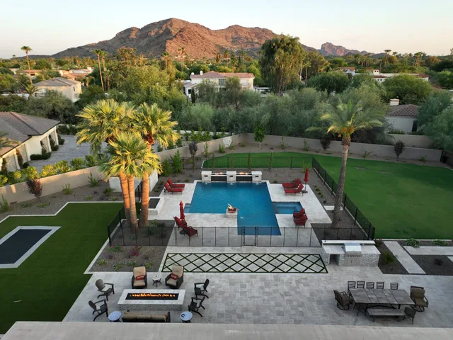 Pools and outdoor living: Aerial view of a rectangular pool with a fire pit, turf and palms below a mountain
